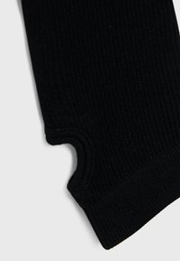 Gros plan sur un tissu en tricot côtelé noir avec un trou pour le pouce, probablement une partie d'une manche ou d'un gant.