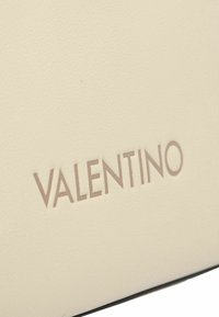 Cuero texturizado en tono crema con el logo "VALENTINO" en relieve en un tono claro. La superficie presenta un sutil patrón granuloso para mayor profundidad.