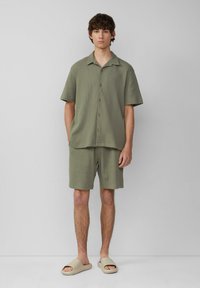 Helles grünes kurzärmeliges Hemd mit Knöpfen und passenden Shorts, aus strukturiertem Stoff, lässige Passform, kombiniert mit beigen Slip-On-Sandalen.
