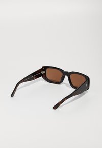 Occhiali da sole marrone con montatura a tartaruga nera e marrone. Lenti rettangolari larghe e bracci snelli e affusolati.