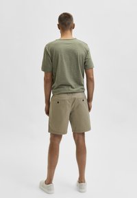 Olivrandig t-shirt och beige shorts med bakfickor. Modellen bär vita skor. En enkel, avslappnad design med en lös passform.