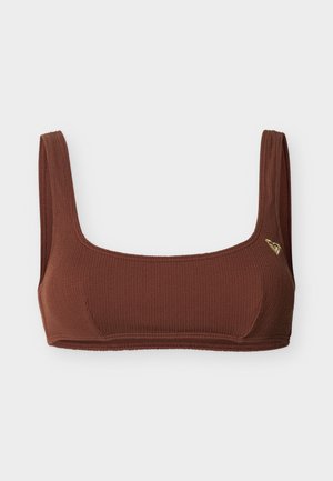 Haut court en tissu texturé marron avec de larges bretelles et un petit emblème en forme de cœur doré sur le côté gauche.