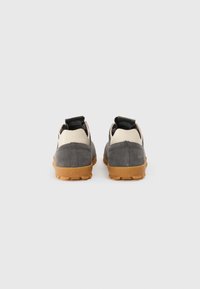 Chaussures en daim gris avec un panneau beige, semelle en caoutchouc et tirant noir à l'arrière. La semelle extérieure présente un motif de bande de roulement robuste.