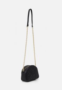 Black quilted crossbody bag with gold chain strap and top zipper, featuring an embossed "M" logo on the front.