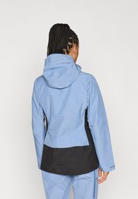 Μπλε αδιάβροχο μπουφάν με κουκούλα, με μαύρη κάτω πάνελ και υφή υφάσματος. Με φερμουάρ στις πλαϊνές τσέπες και ρυθμιζόμενους καρπούς.