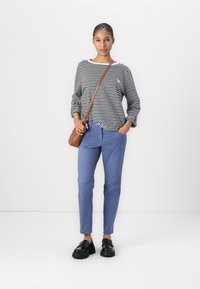 Camicia a righe a maniche lunghe con polsini svasati, pantaloni blu e mocassini neri spessi. Una borsa a tracolla marrone aggiunge un accento di contrasto.