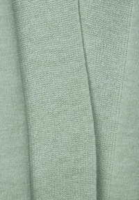 Ljusgrön stickad tyg med ett texturerat mönster; mjuk att ta på och med en subtil lyster. Flera veck skapar djup.