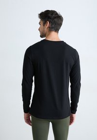 Svart langermet skjorte med rund hals, glatt tekstur og tettsittende design, brukt med grønne leggings. Enkelt og minimalistisk stil.