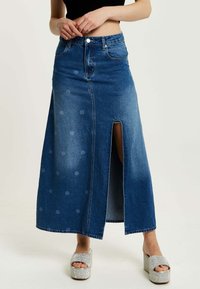 Denim maxi skirt featuring a front split, light dot pattern, and a high waist design. Paired with silver platform shoes.