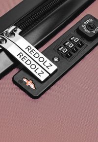 Maleta de viaje rígida en rosa con acabado texturizado, que cuenta con un doble cierre con tiradores de metal y un candado de combinación con detalles en negro.