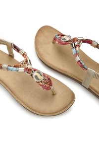 Sandales en suédine synthétique marron avec des lanières tressées multicolores et des accents métalliques. Présente un emblème circulaire au niveau de la jonction entre les lanières.