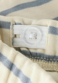 Gestreepte stof in lichtbeige en lichtgrijs, met een gestructureerd oppervlak. Witte knoopsluiting met horizontale openingen, gedetailleerde stiksels zichtbaar.