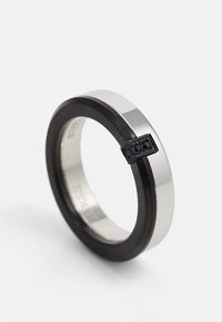 Silver and black metal ring with embedded black stones on a white background, slightly tilted upright.