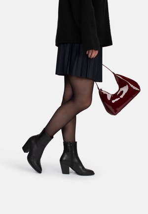 Black leather ankle boots with a pointed toe and chunky heel, paired with a pleated black skirt and a glossy burgundy handbag.