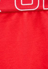 Κοντινό πλάνο κόκκινου υφάσματος με ραφή και μερικώς ορατό κείμενο με λευκά ράμματα στην άνω άκρη.