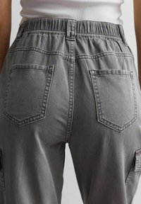 Bakvy av grå denimbyxor med elastisk midja och två bakfickor, kombinerat med en vit ribbad topp.