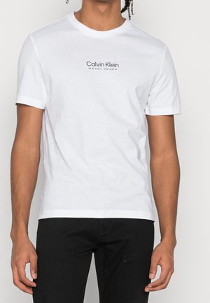 Hvid bomulds t-shirt med korte ærmer og rund halsudskæring. Har "Calvin Klein" tekstlogo på brystet i marineblå, enkel design.