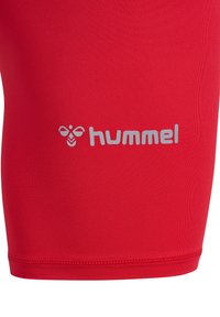 Røde sportskort lavet af glat, strækbart stof, med et hvidt "hummel" logo og et bi-emblem på den nederste side.