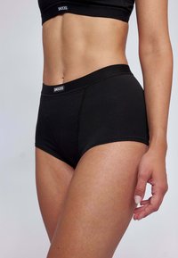 Shorts en boyshort taille haute noirs en tissu doux, avec un logo sur la ceinture, et un design sans coutures qui procure du confort.