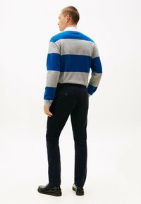 Polo a maniche lunghe a righe grigie e blu, abbinato a pantaloni blu scuro. Tessuto misto cotone, morbido al tatto e dal taglio rilassato. Scarpe nere.