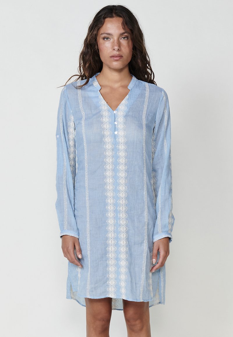 Helles blaues Leinenkleid mit V-Ausschnitt, langen Ärmeln und weißen bestickten Akzenten an der Vorderseite und den Ärmeln, mit Seitenschlitzen.