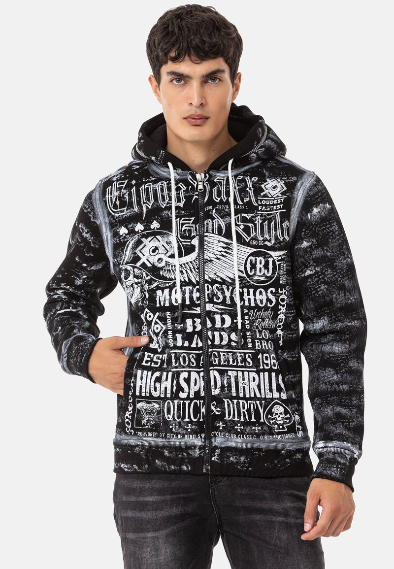 Schwarze Zip-Hoodie mit weißem Grafiktext und Designs, einer Kordelzugkapuze, Fronttaschen und einem strukturierten Stoff mit einem verblassten Muster.