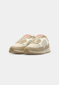 Beige sneakers with a textured mesh upper, suede accents, and a cushioned sole. Features pink branding on the tongue and side.