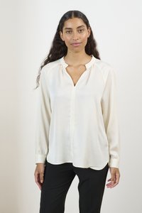 Langærmet, elfenbensfarvet bluse med V-udskæring og draperinger ved skuldrene, der har en glat tekstur og en let buet kant.
