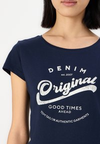 Marineblå bomulls t-skjorte med hvitt grafisk design som har teksten: "DENIM Original est. 2007" og "Good Times Ahead" i en uformell stil.