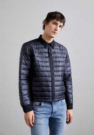 Navy blue padded jacket with a collar, front zipper, and ribbed cuffs. Features a quilted texture with smooth side panels.