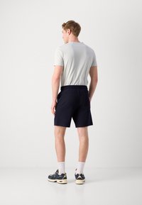 Mann i lys grå, kortermet skjorte og mørk marineblå shorts. Shortsene har elastisk midje og lommer. Joggeskoene er marineblå med detaljer.