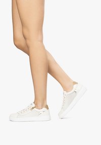 Baskets blanches avec des accents en maille et similicuir, dotées d'une semelle blanche, d'un bout rond et d'œillets dorés. Motif texturé sur les côtés.