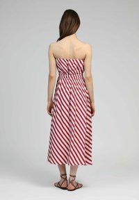 Robe sans bretelles avec des rayures diagonales rouges et blanches, taille élastique, jupe fluide et ourlet longueur cheville. Portée avec des sandales plates à lanières.