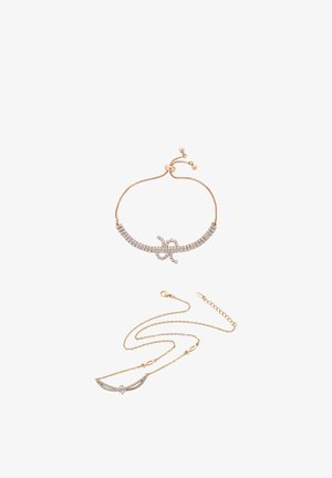 Deux colliers en ton or avec strass clairs ; un bracelet ajustable avec détail en forme de nœud, un collier à chaîne avec pendentifs en forme d'aile et de cœur.