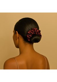 Fascia per capelli in raso color bordeaux con design arricciato, che adorna un'acconciatura a chignon liscio e scuro. Superficie texturizzata e lucida.