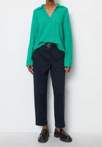 Green cable-knit sweater with a V-neck and collar, paired with navy trousers, and black slip-on shoes featuring chunky soles.