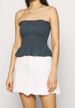 Mujer con un top negro sin tirantes fruncido con dobladillo de volantes, combinado con una minifalda de mezclilla blanca con bordes deshilachados.