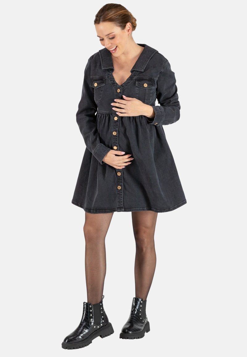 Schwarzes Denimkleid mit V-Ausschnitt, großem Kragen, Knopfverschluss und gerafftem Taillenbereich. Kombiniert mit knöchellangen schwarzen Stiefeln mit Nieten.