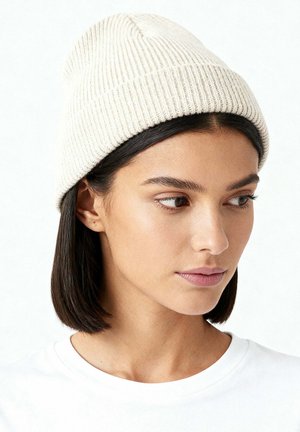 Bonnet tricoté beige avec une texture côtelée, présentant un revers retroussé. Matière douce, forme ajustée et design minimaliste.