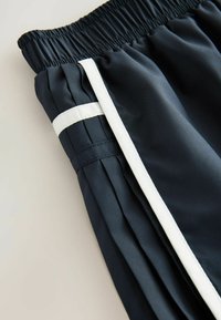 Marineblauwe sportshorts met een elastische tailleband, voorzien van een witte zijstreep en subtiele plooidetails langs de naad voor extra textuur.