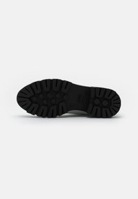 Suela de zapato de goma negra con un patrón de tracción robusto, que presenta diseños circulares y rectangulares para mejorar la tracción y la durabilidad.