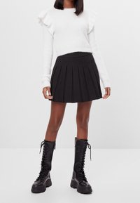 White, fluffy sweater with ruffled sleeves; black pleated mini skirt; mid-calf black lace-up boots with chunky soles.