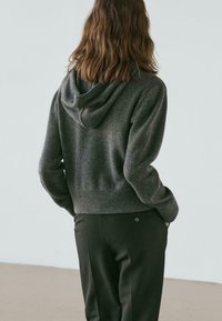 Cropped grey hoodie made of soft knit fabric, featuring a drawstring hood and ribbed hem, paired with dark trousers.