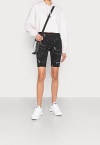 Svarta cykelshorts med ett virvlande Nike-mönster, som är ihop med en ljusrosa croppad hoodie och vita sneakers. Outfitten inkluderar en liten axelväska.