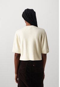 Cremefarbenen, kurzärmeligen Pullover mit bequemer Passform, rundem Ausschnitt und geripptem Saum. Kombiniert mit einem braunen Cordrock mit Tasche auf der Rückseite.