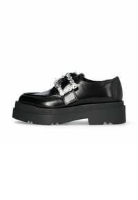Black patent leather shoe with a chunky black platform and decorative rhinestone buckle. Features fur accents and textured rubber sole.