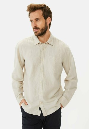 Lys beige skjorte med knapper lavet af et blødt, tekstureret stof. Har en brystlomme, klassisk krave og lange ærmer.