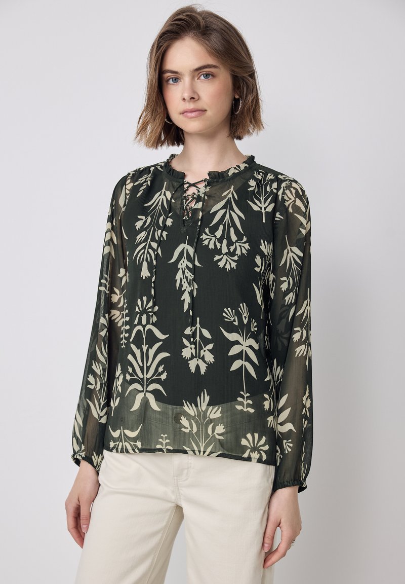 Langärmlige Bluse aus dunklem grünen, transparentem Stoff mit crèmefarbenen Blumenmustern, einem Rüschenausschnitt und einer Schnürung an der Vorderseite.