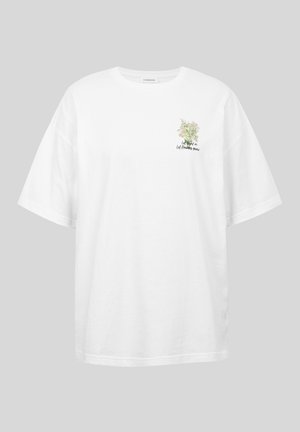 T-shirt blanc oversize avec petit motif floral et texte « Laisse entrer la lumière, laisse pousser les fleurs » sur la poitrine gauche.