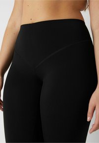 Höga svarta leggings med en mjuk, stretchig textur, med en V-formad sömdetalj vid midjan för konturformning.